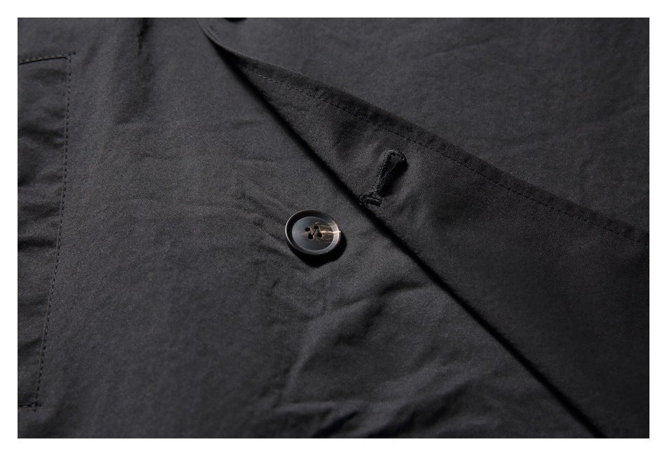 Close-up of a black coat button and buttonhole beneath the overlapping front placket.