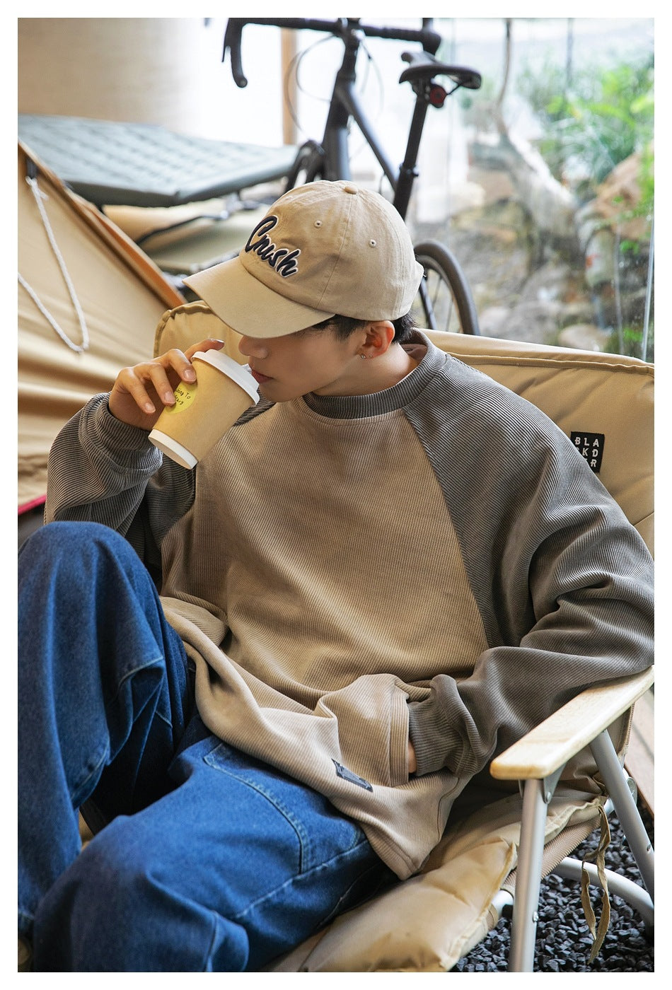 Seated model wearing a beige sweatshirt with gray raglan sleeves and ribbed cuffs.