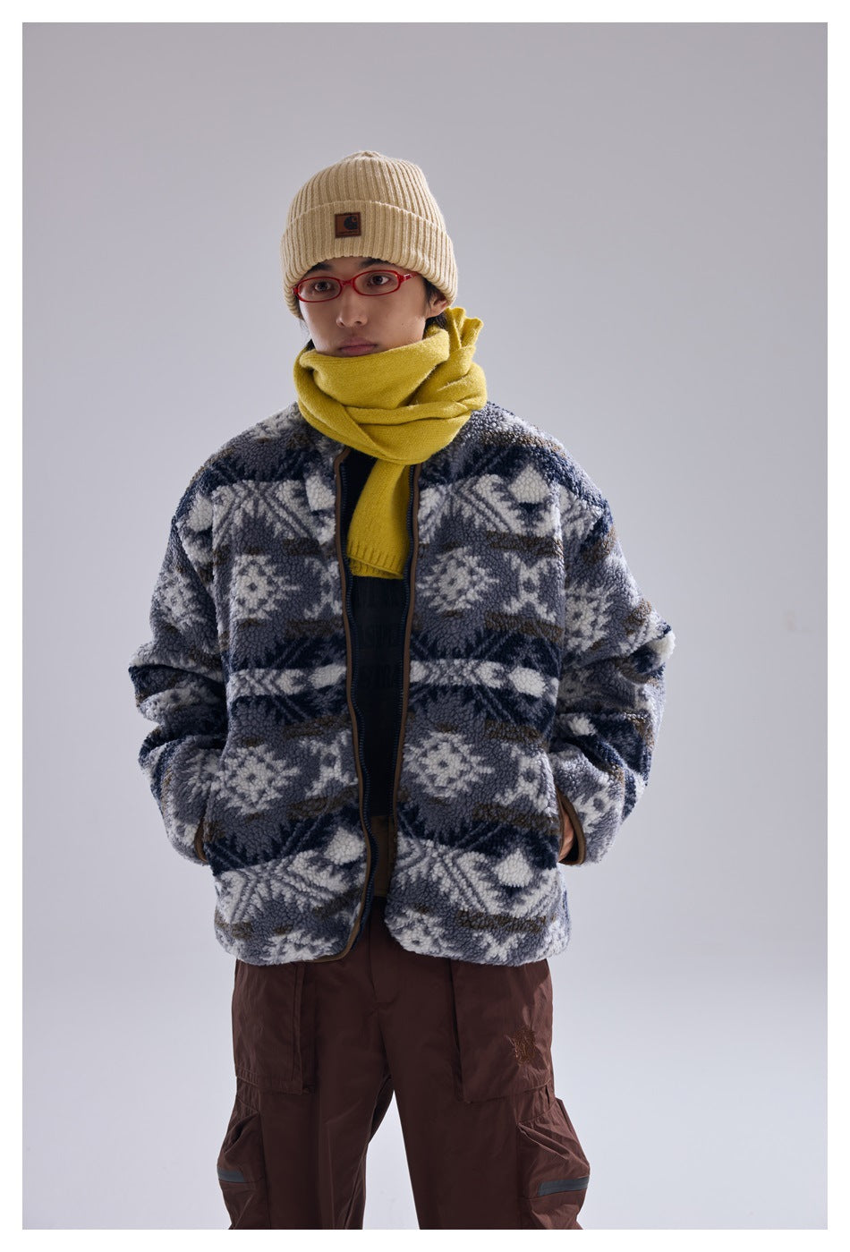 Model in a gray, navy, and cream patterned fleece jacket, yellow scarf, and beige beanie, shown from the front.