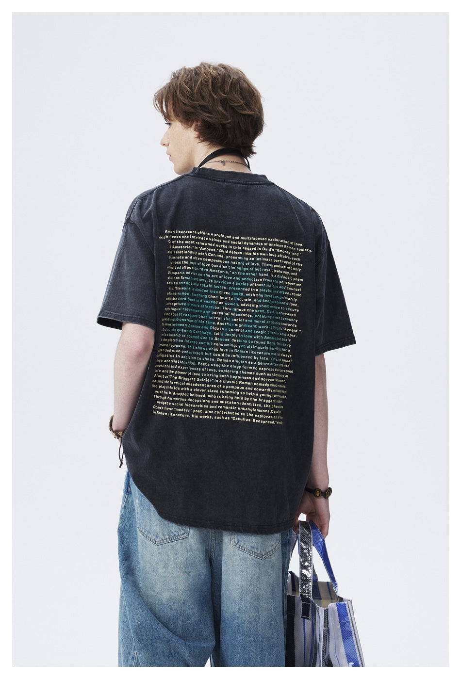 Back view of a model wearing a dark oversized T-shirt with a large block of light-colored text and blue jeans.