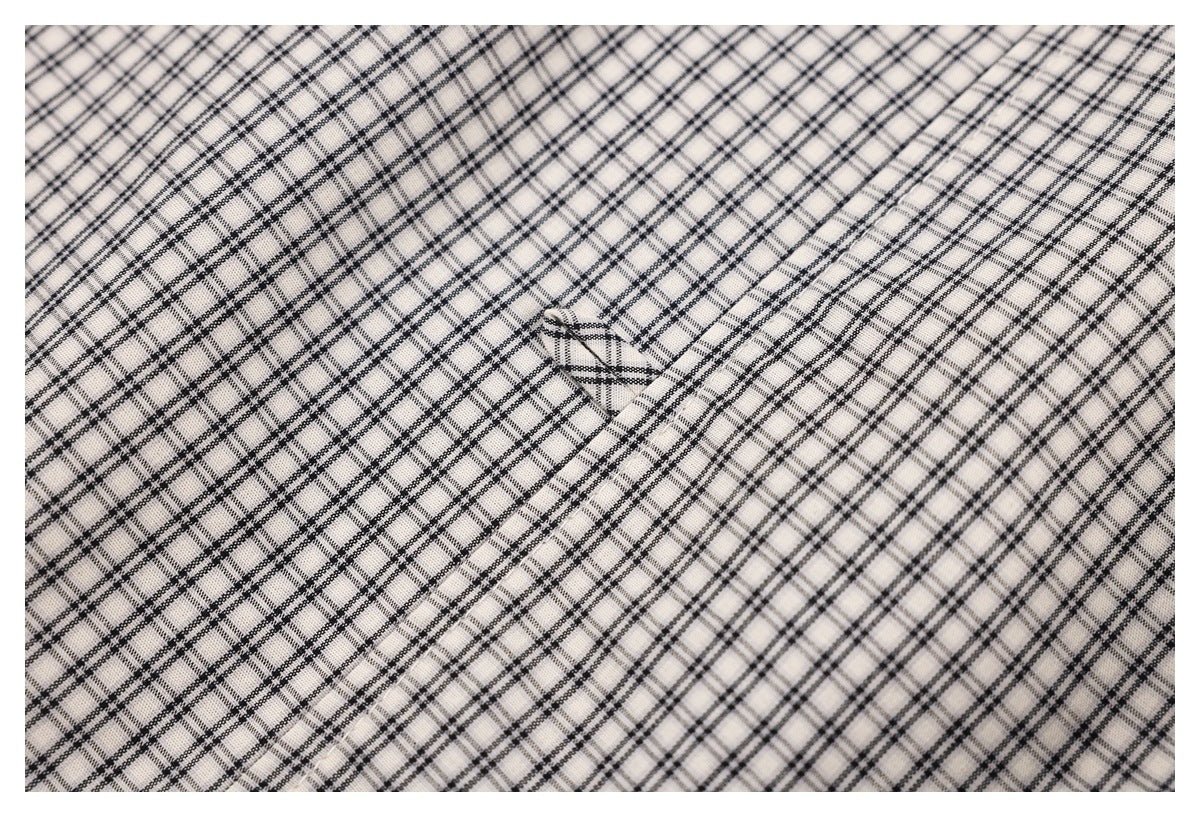 Close-up of cream fabric with a fine black checked pattern and a small folded opening.