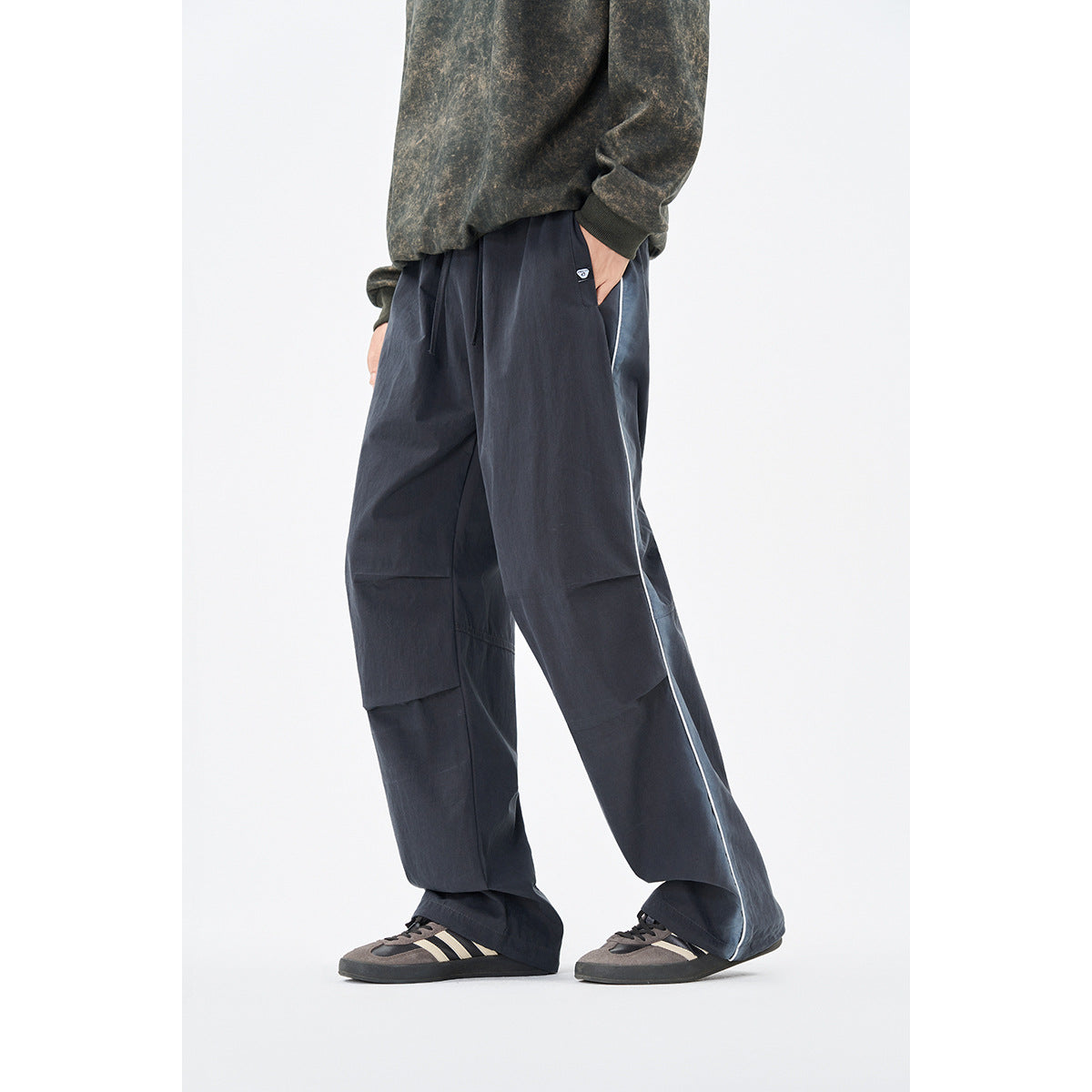 Model wearing loose dark charcoal trousers with a pale side stripe and articulated knee panels, shown at an angle.
