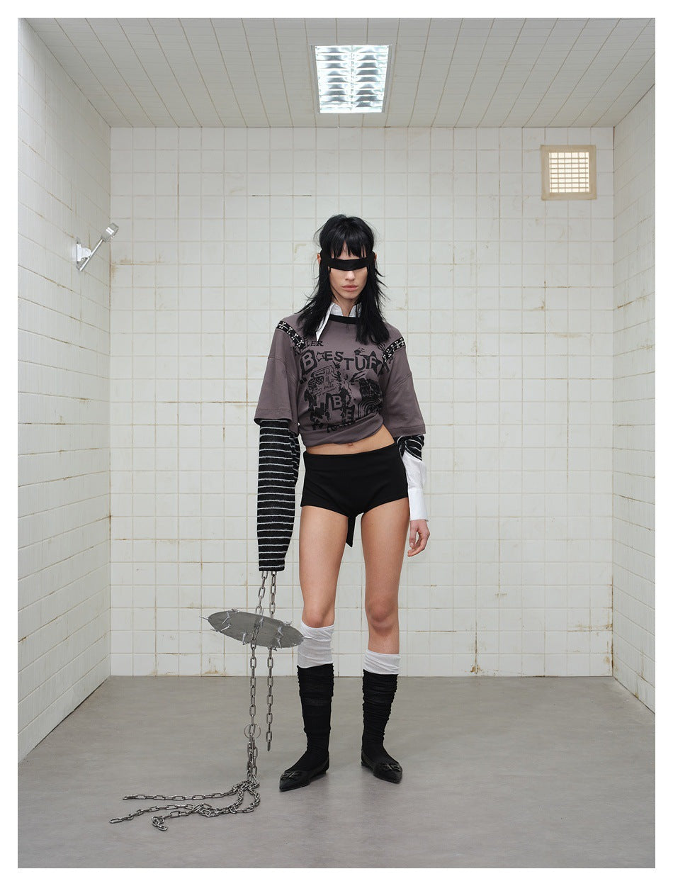 Model standing in a tiled room wearing the gray graffiti faux two-piece top with striped sleeves and black shorts