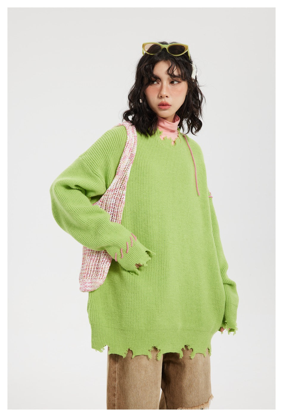 Front view of a model in an oversized lime-green distressed sweater with pink accents and brown trousers.