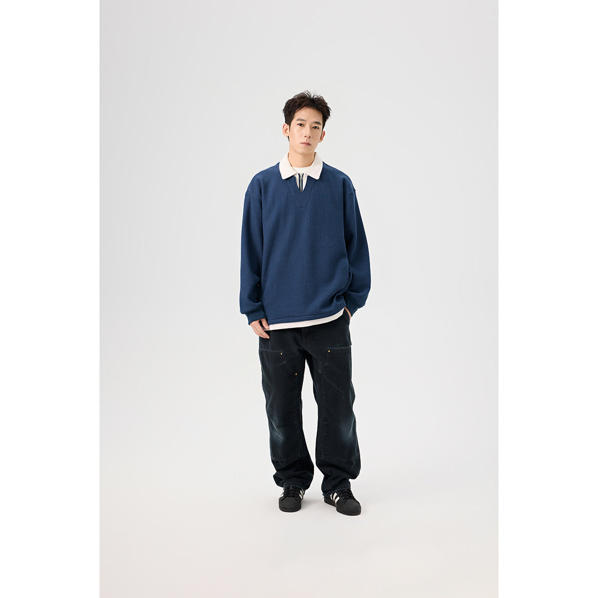Model wearing a navy pullover with a white collar and short zip placket, styled with black loose-fit pants.