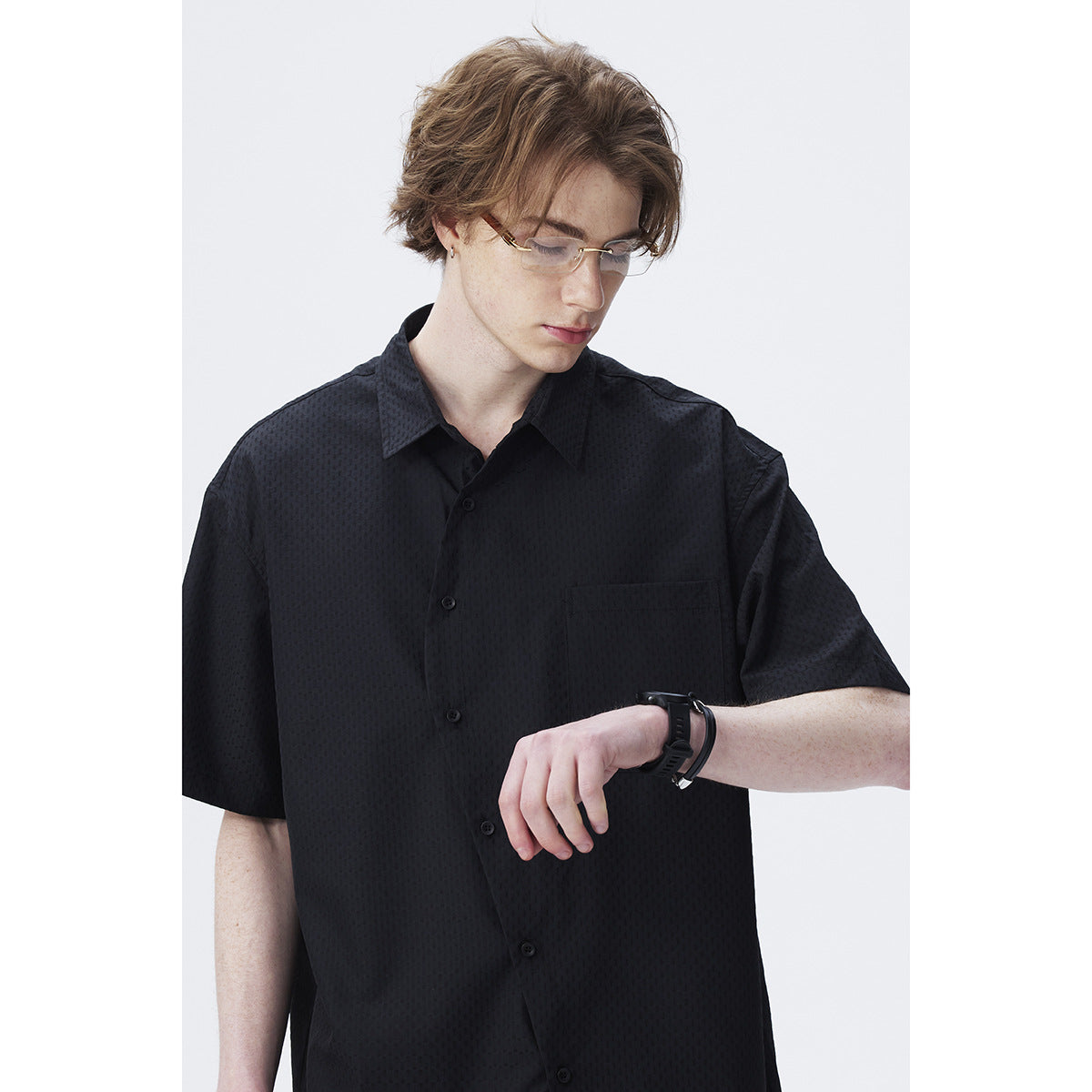Close-up of a black short-sleeve button-up shirt, showing its subtle textured pattern, buttons, collar, and chest pocket.