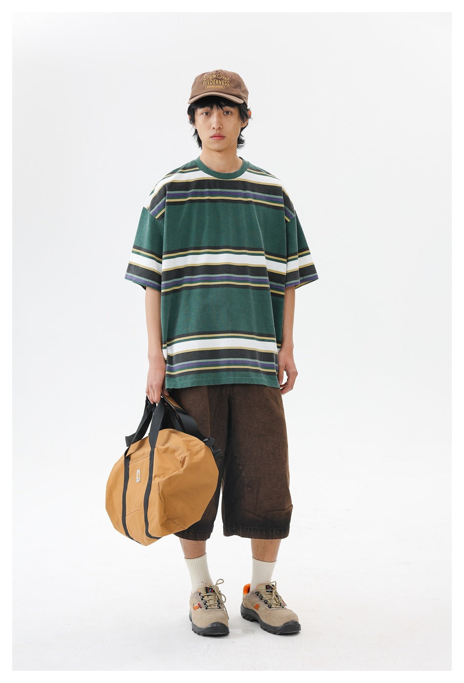 Front view of a model wearing a forest-green striped oversized T-shirt and carrying a tan duffel bag.