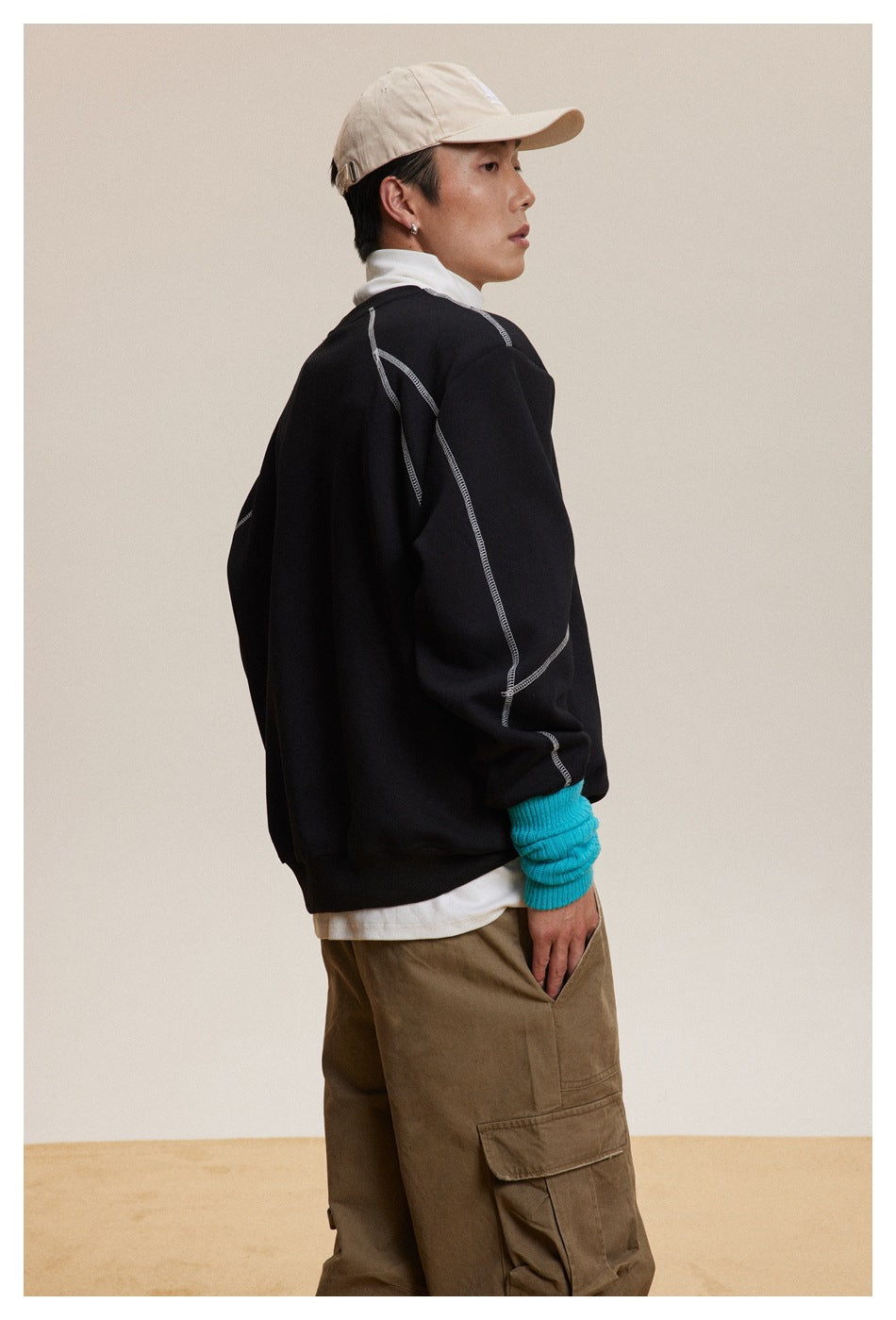 Side and partial back view of a model wearing a black sweatshirt with white contrast seams.