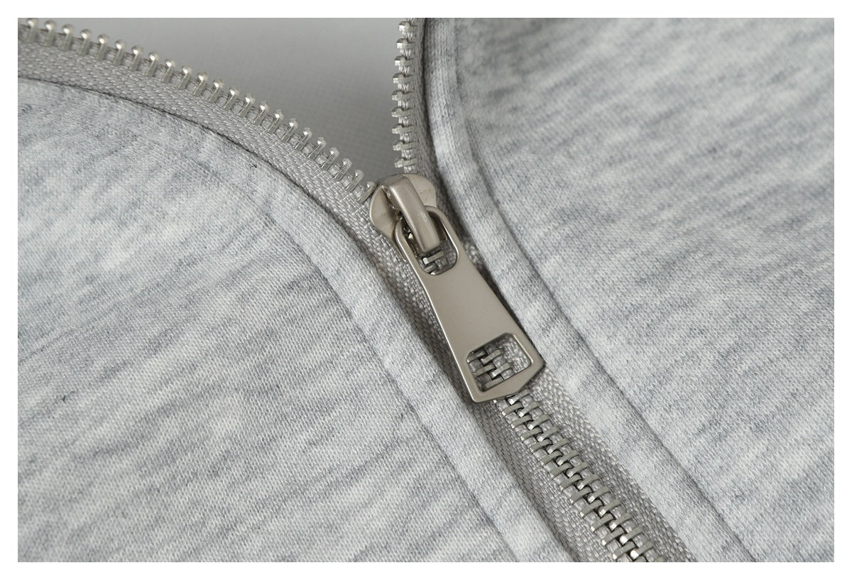 Close-up of the silver zipper slider and teeth on light gray heather fabric.