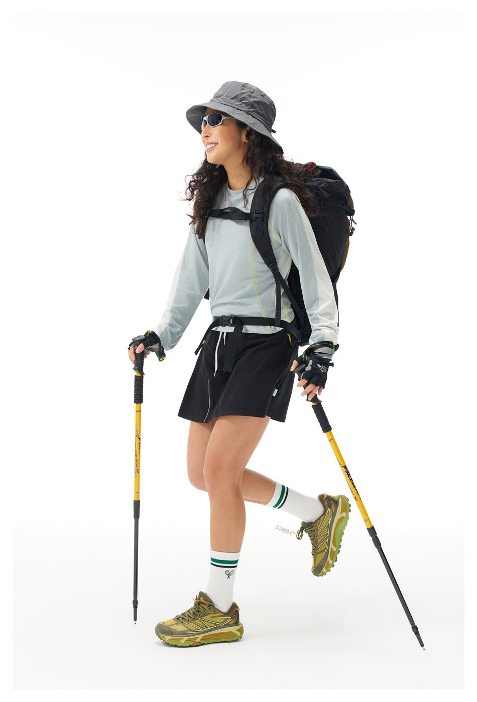 Side view of a model wearing a pale gray long-sleeve top and black skort with a hiking backpack and poles.