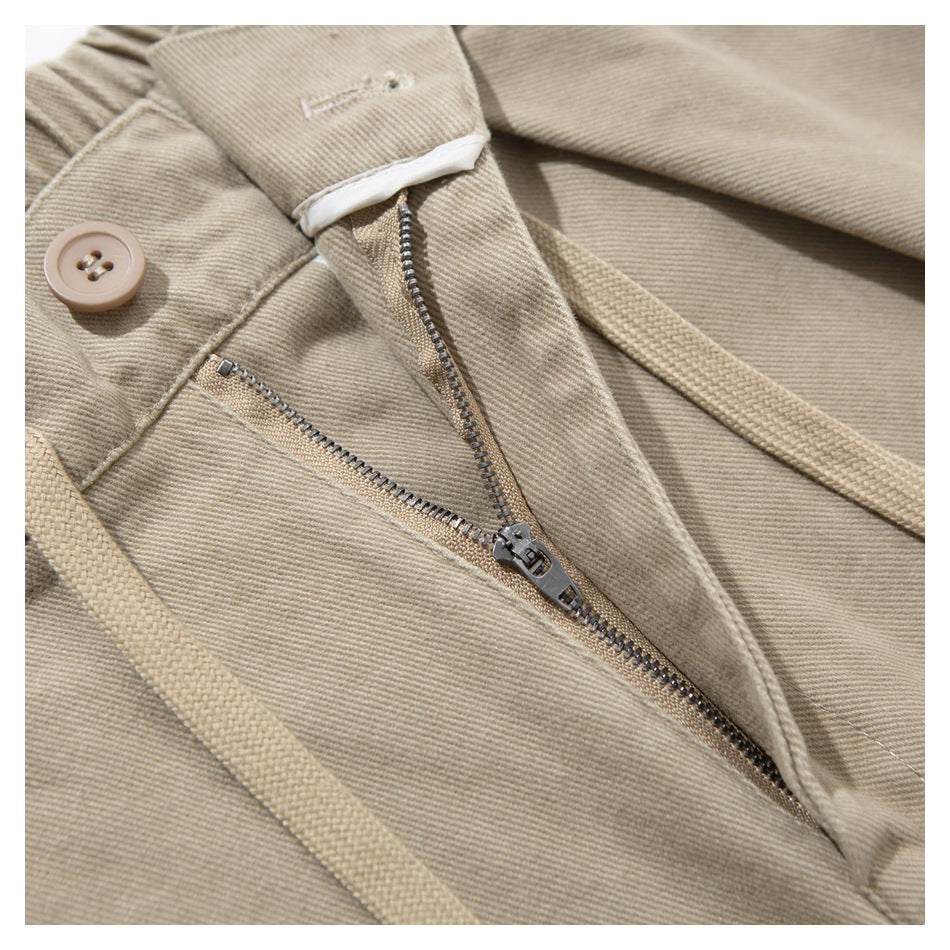 Close-up of beige trousers showing the button, partly open zipper, and waist tie.