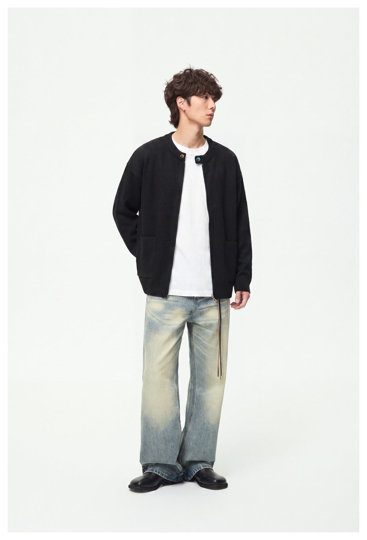 Model wearing a black knit zip cardigan open over a white tee with faded light-wash wide-leg jeans and black shoes
