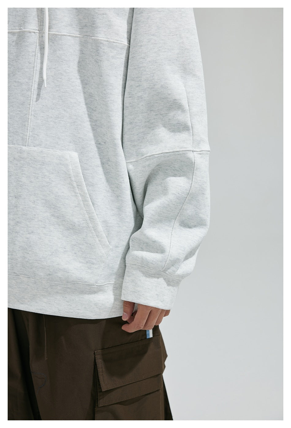 Close-up of the light gray sweatshirt's pocket, sleeve paneling, and cuff.