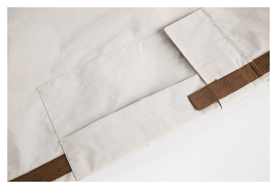 Close-up of light beige trousers with a brown woven trim and stitched panel.
