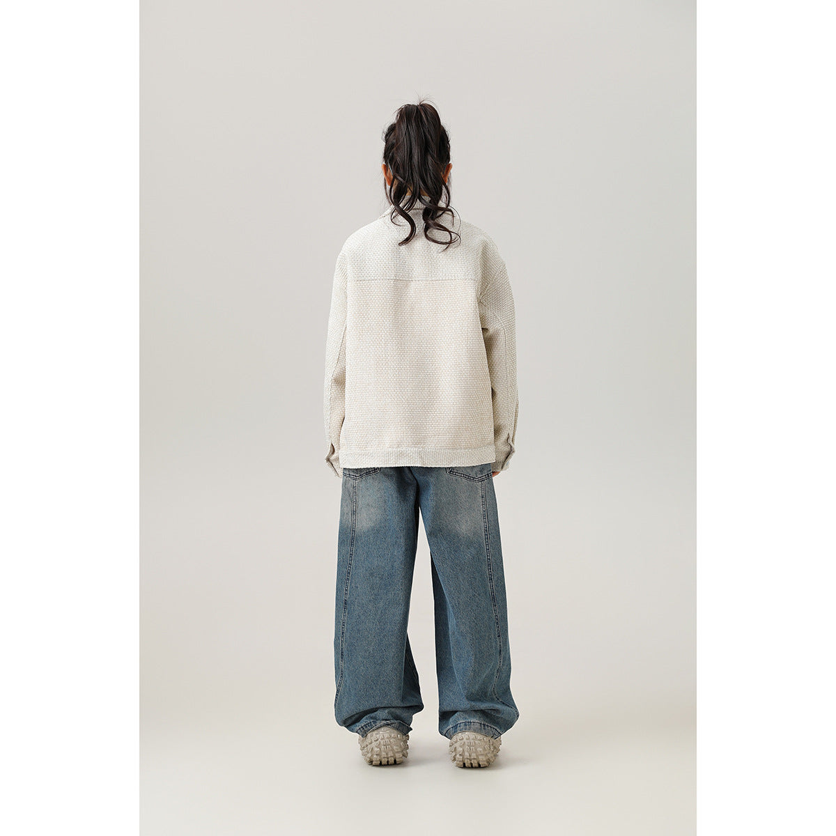 Back view of a model wearing a plain cream jacket and loose blue jeans.