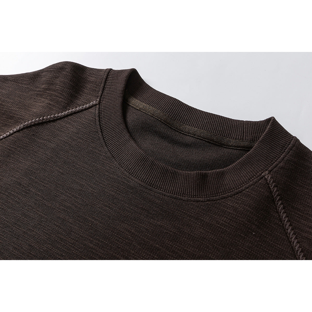Close-up of a dark brown crewneck sweatshirt showing the ribbed collar and raglan shoulder seams.