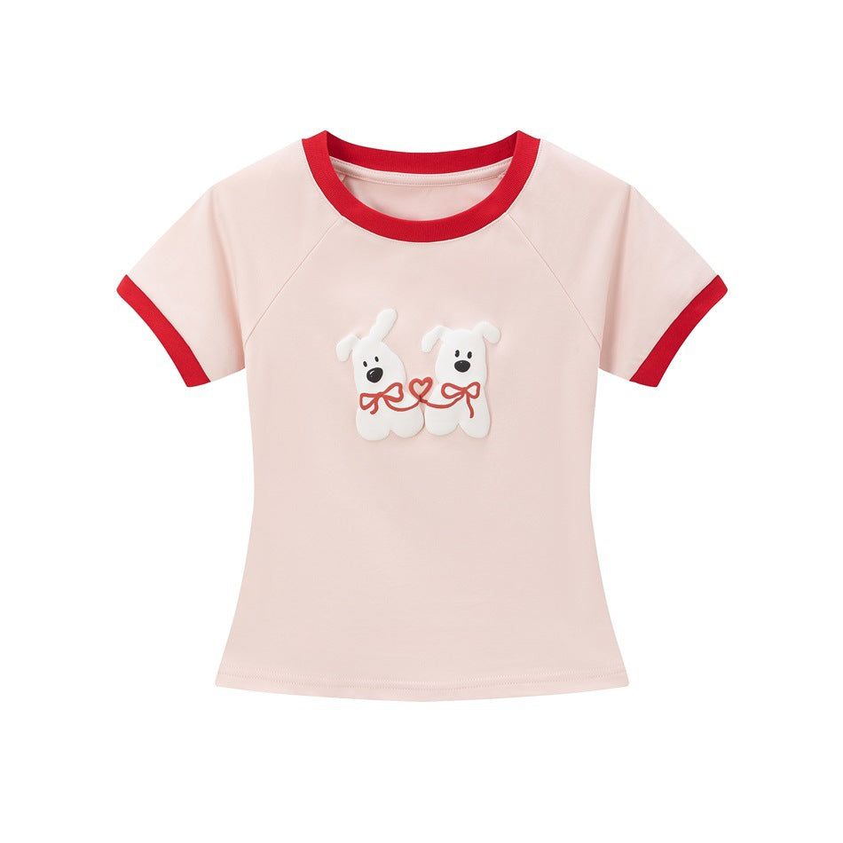 Pink short-sleeve cropped tee with red neck and cuff trim and a raised two-dog graphic with red bows on the front