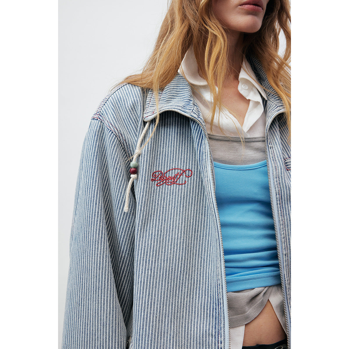 Close-up of the pinstriped jacket showing its collar, zipper, chest pocket, drawcord detail, and red embroidery.