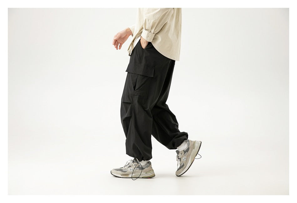 Side view of a model wearing loose black cargo pants with layered flap pockets and gathered ankles.