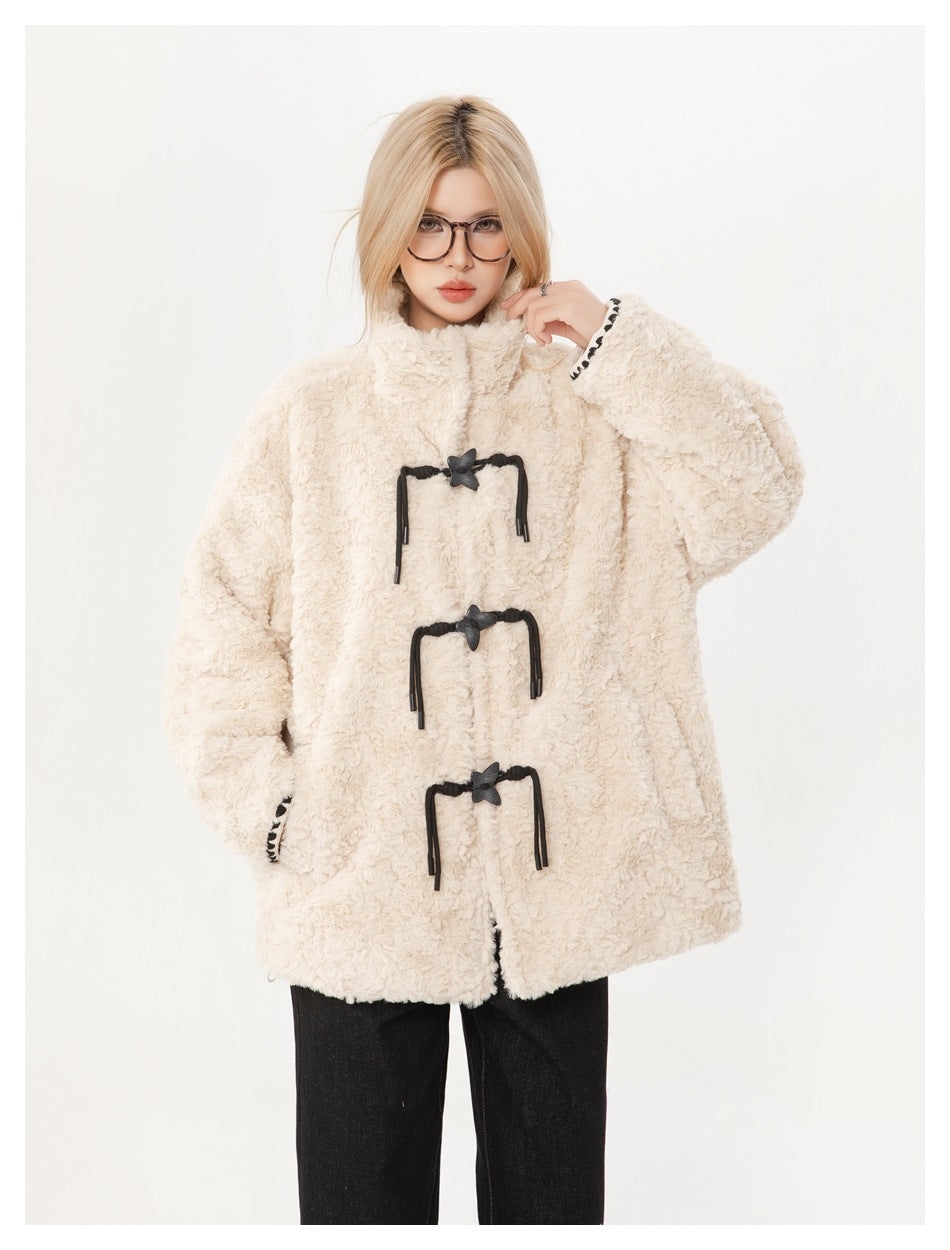 Model wearing an ivory plush toggle coat with a high collar and black trousers, front view with one hand raised.