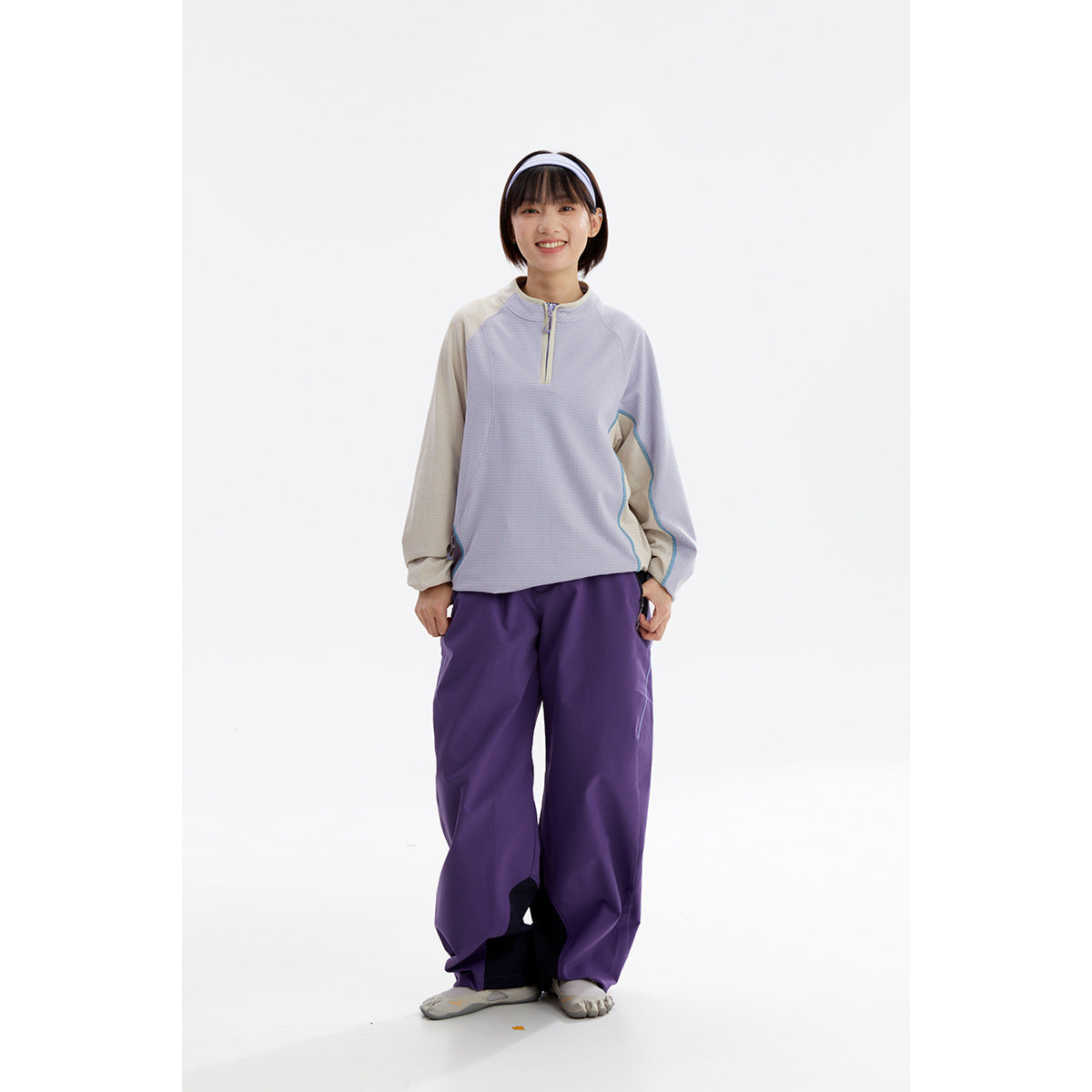Front view of a model wearing a light lavender quarter-zip top with beige sleeves and loose purple pants.