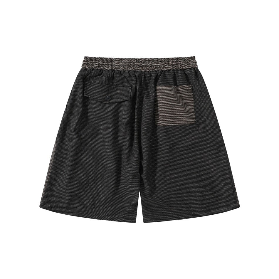 Back view of black textured shorts with a button flap pocket and a brown-gray patch pocket