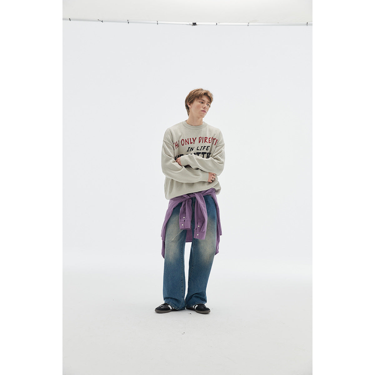 Model wearing a light gray slogan sweatshirt, wide-leg blue jeans, and a purple shirt tied at the waist.