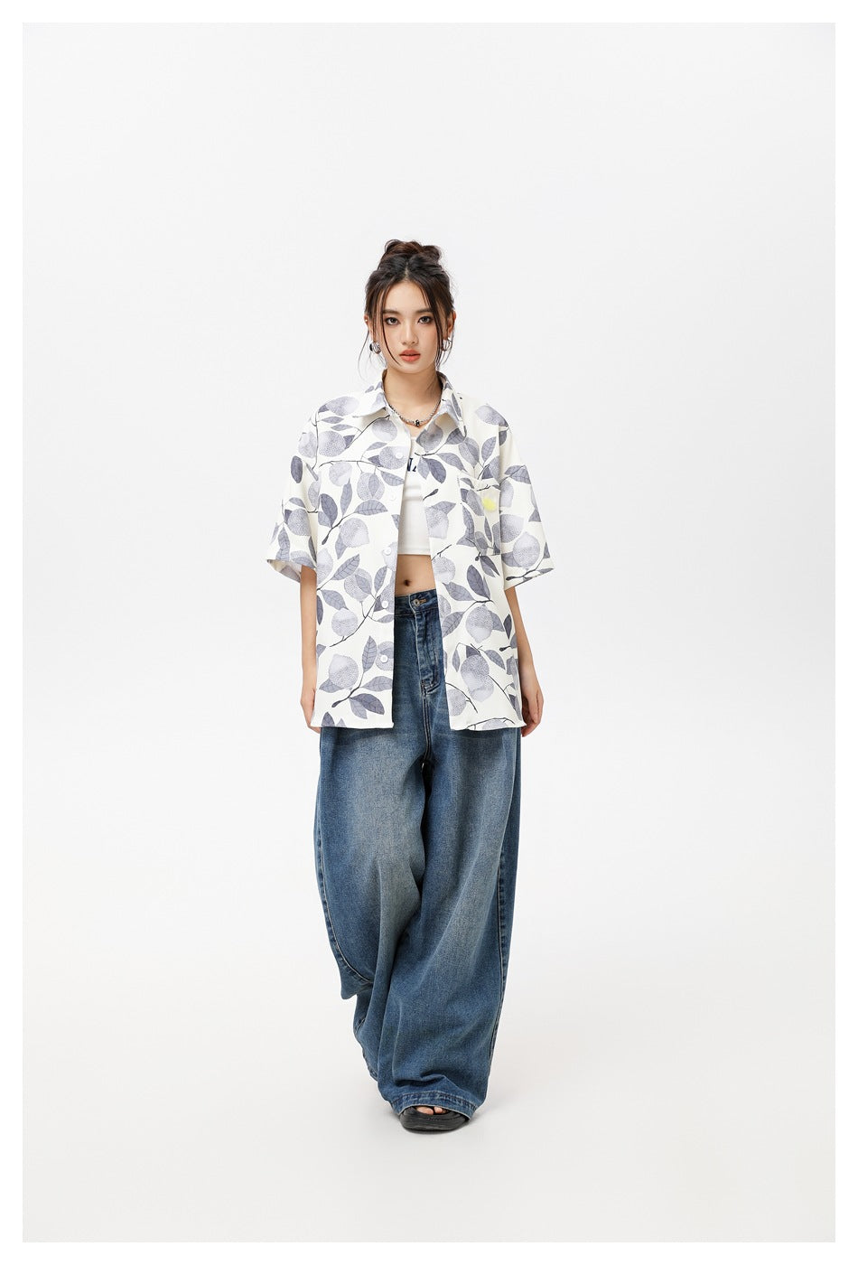 Model wearing an ivory short-sleeve button-up shirt with a gray botanical print, paired with wide-leg blue jeans.