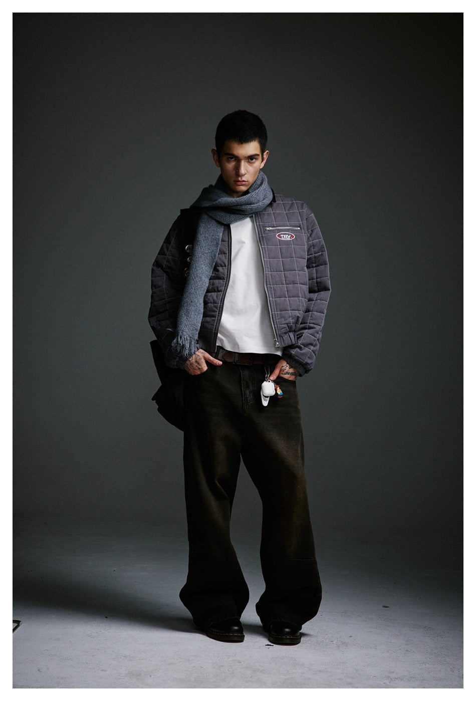 Full-length model wearing a gray grid-quilted jacket, long scarf, white shirt and dark wide-leg trousers.