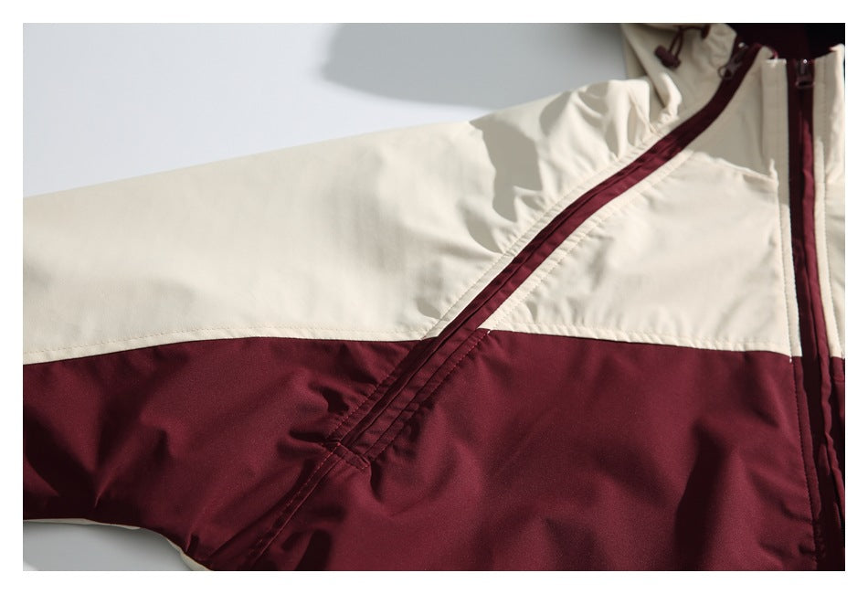 Close-up of a cream and burgundy jacket showing a diagonal seam and color-blocked sleeve.