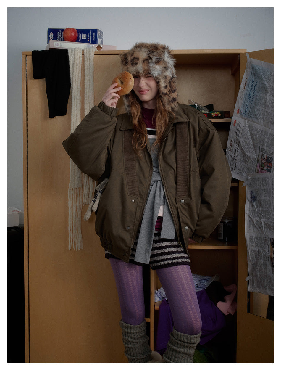 Model wearing an oversized olive-brown jacket with ribbed panels and a spotted faux-fur trapper hat.