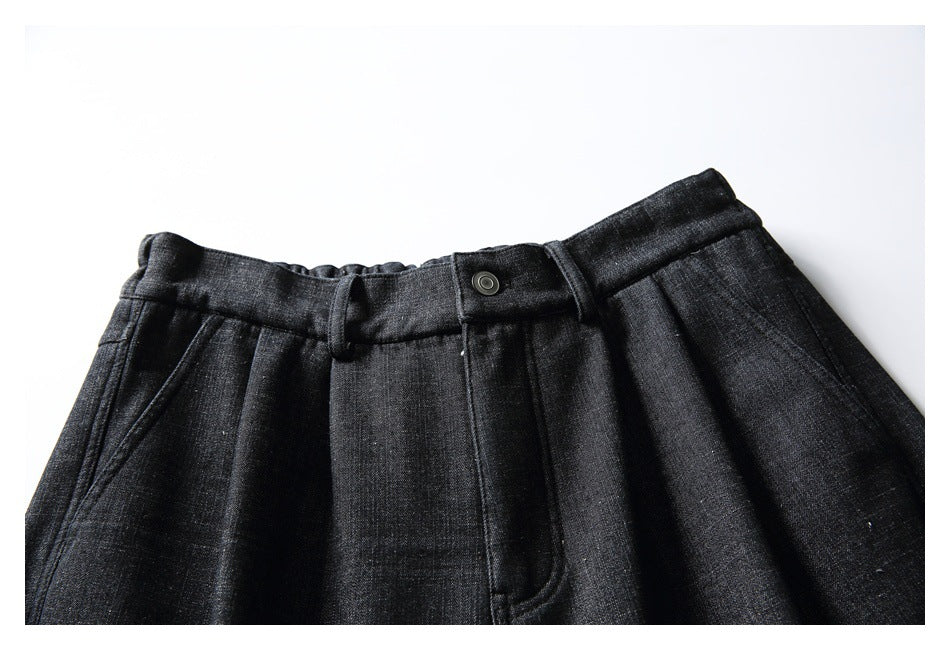 Upper front of charcoal-black trousers with a buttoned waistband, belt loops, pleats and slanted pockets.