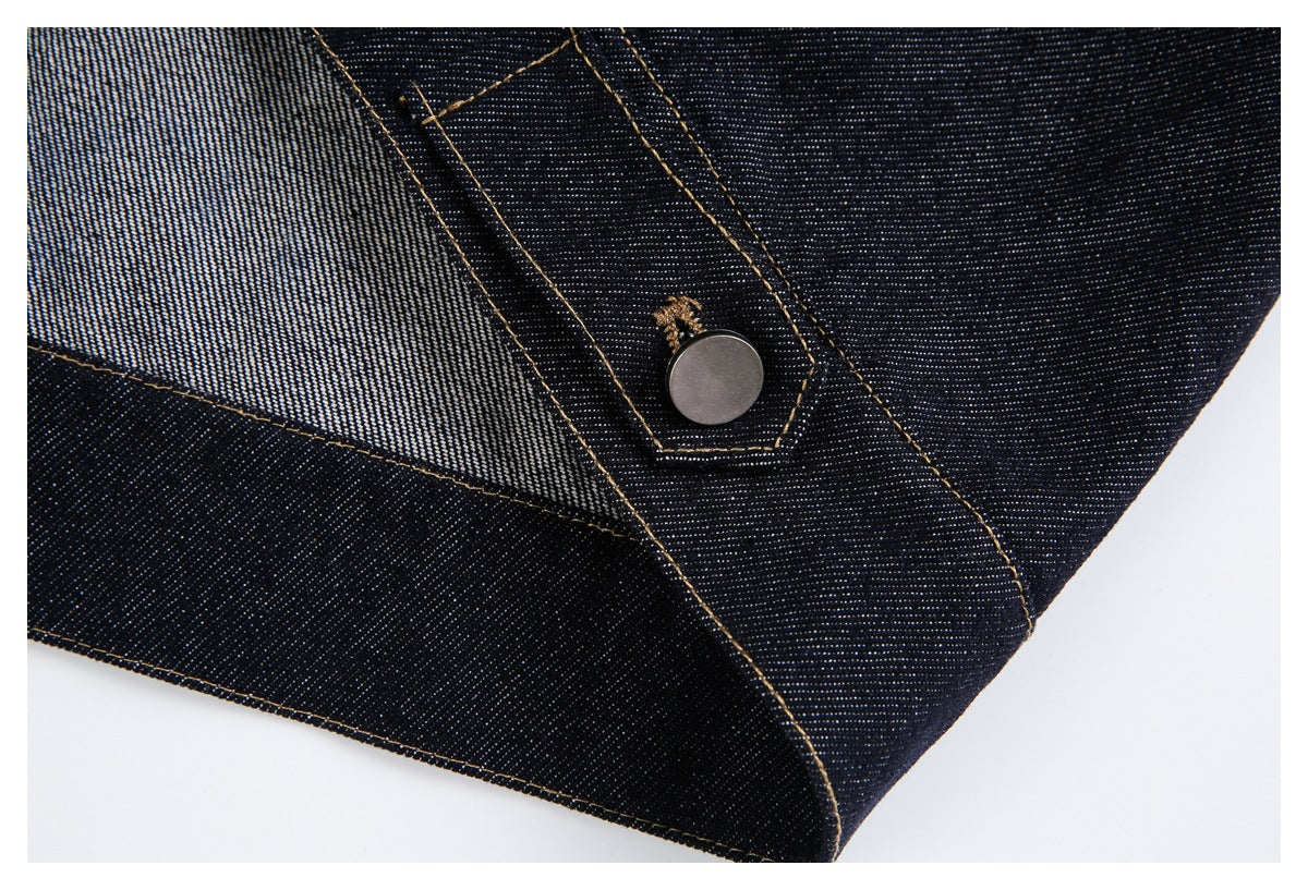 Close-up of a metal button and contrasting tan stitching on dark indigo denim.