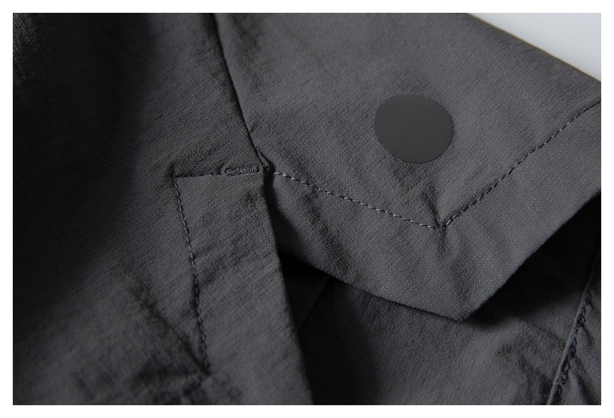 Close-up of a dark charcoal garment showing a stitched flap and round black snap fastener.