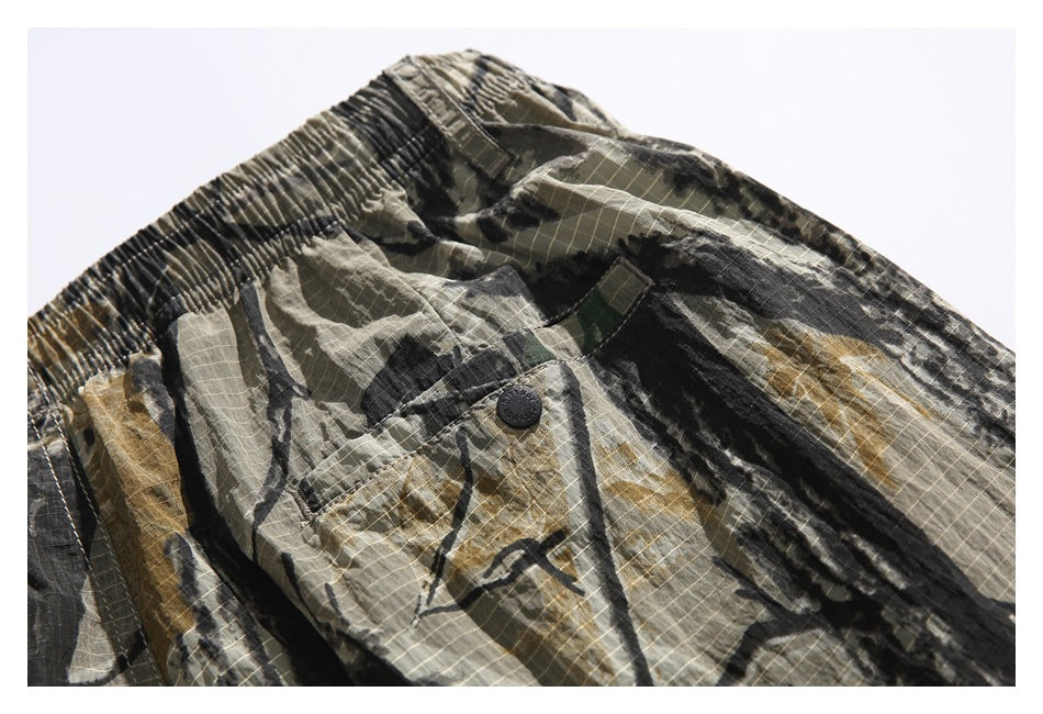 Close-up of camouflage shorts showing the elastic waistband and a buttoned front pocket.