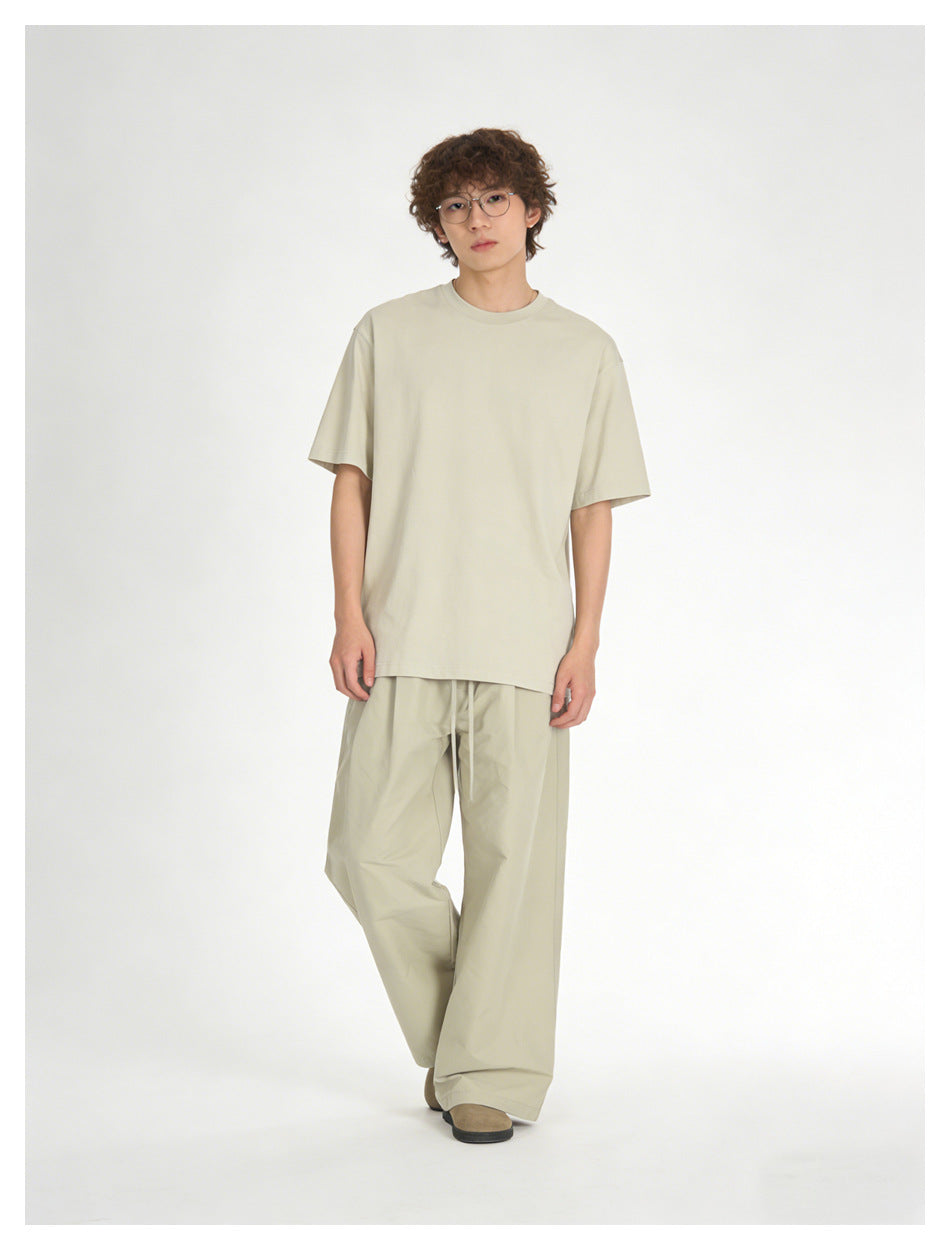 Model wearing a loose light beige T-shirt and wide-leg drawstring trousers, shown from the front.