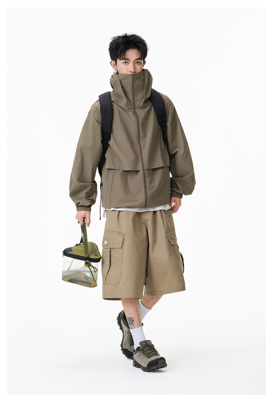 Model wearing an olive-brown hooded zip jacket and tan cargo shorts, with a black backpack.