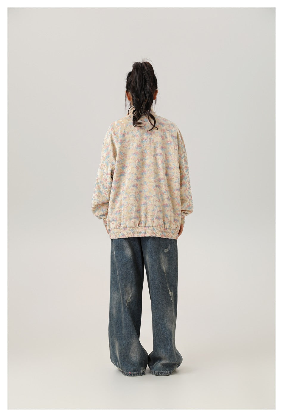 Back view of a model wearing a pastel multicolor zip-up jacket and wide-leg distressed jeans.