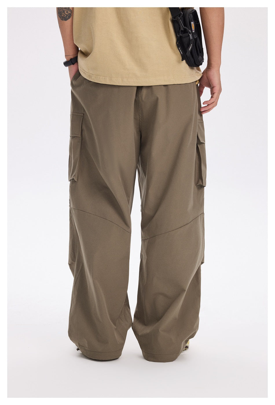 Back view of a person wearing army green wide-leg cargo pants with a tan T-shirt and small black bag
