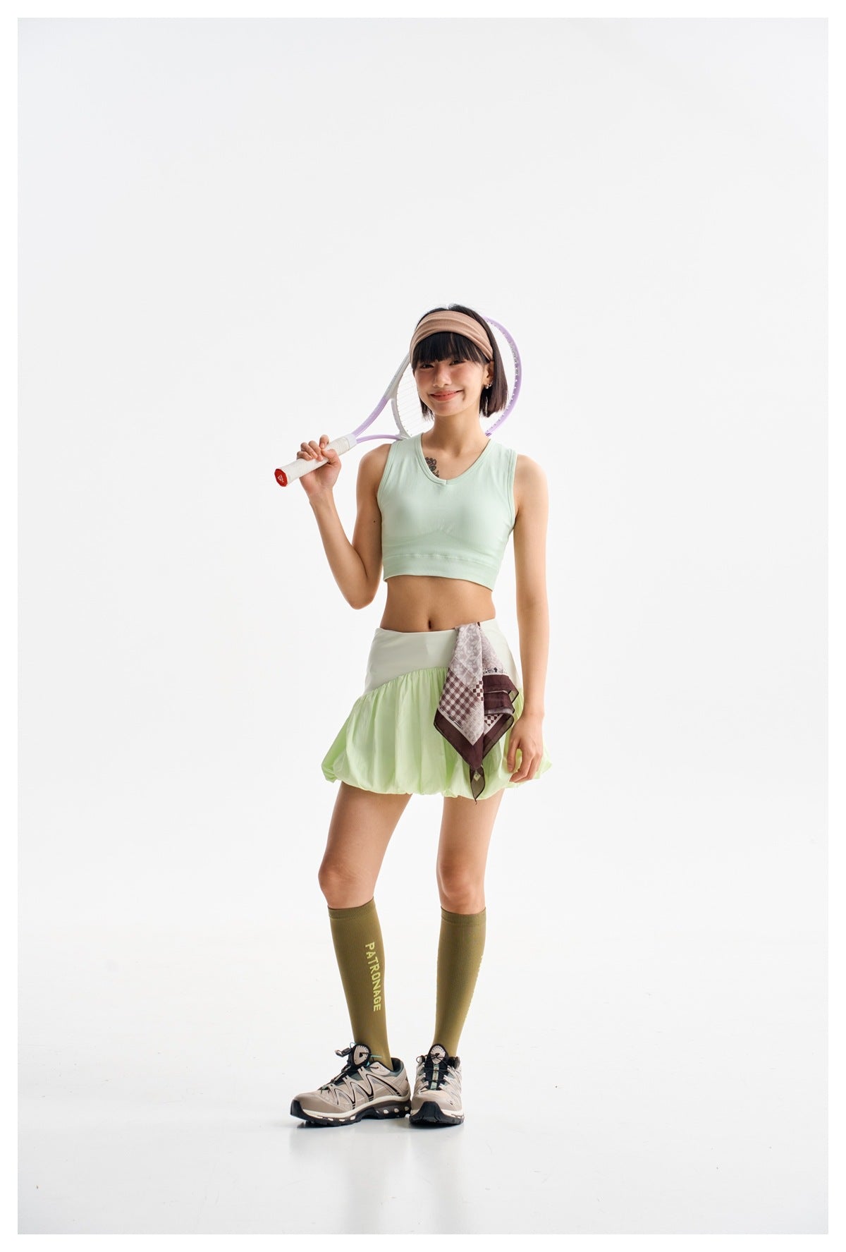 Model wearing a light green bubble-hem mini skort with a green crop tank, holding a tennis racket