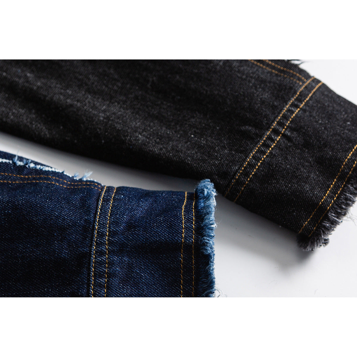 Close-up of dark indigo and black denim sleeve ends with gold stitching and frayed cuffs.