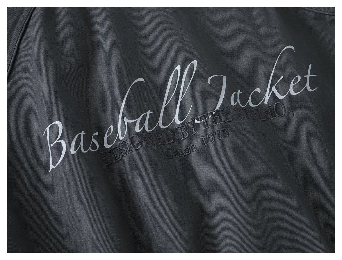 Close-up of dark charcoal fabric with white script reading “Baseball Jacket” and subtle black embroidered lettering.