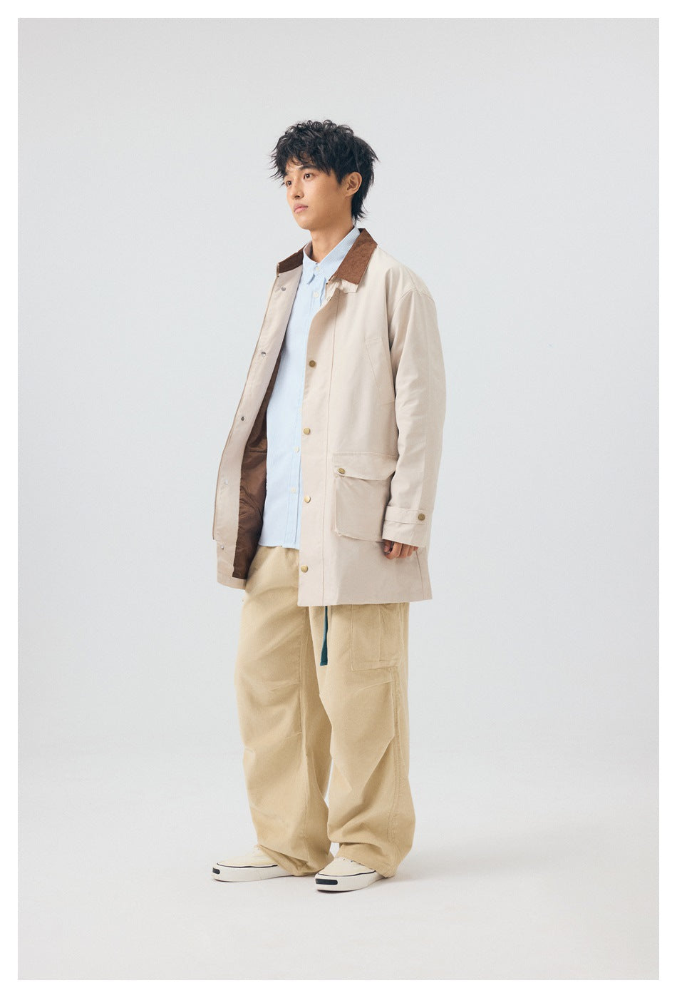 Model wearing an open off-white mid-length jacket with brown collar over a light blue shirt and beige wide-leg pants