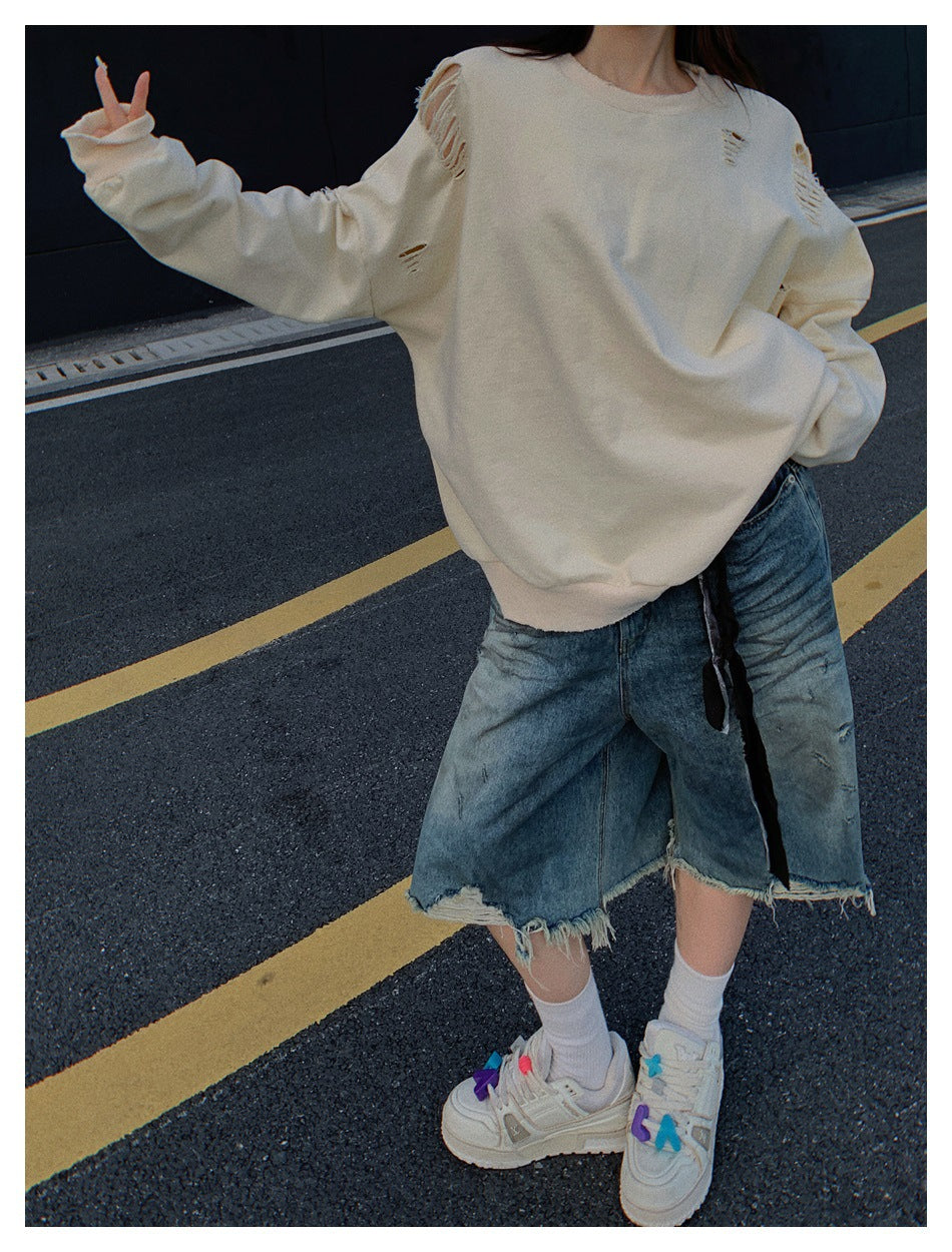 Cropped view of a model wearing a loose cream distressed sweatshirt and frayed denim shorts with white sneakers.