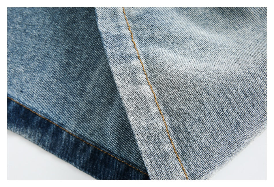 Close-up of contrasting blue denim panels joined by a single line of orange stitching.