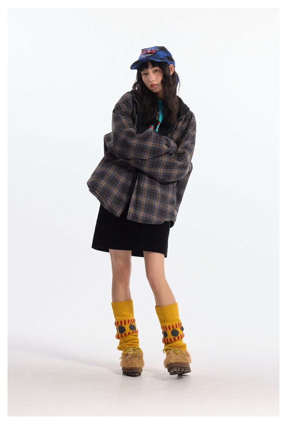 Model with arms crossed wearing oversized plaid hooded jacket over a black skirt