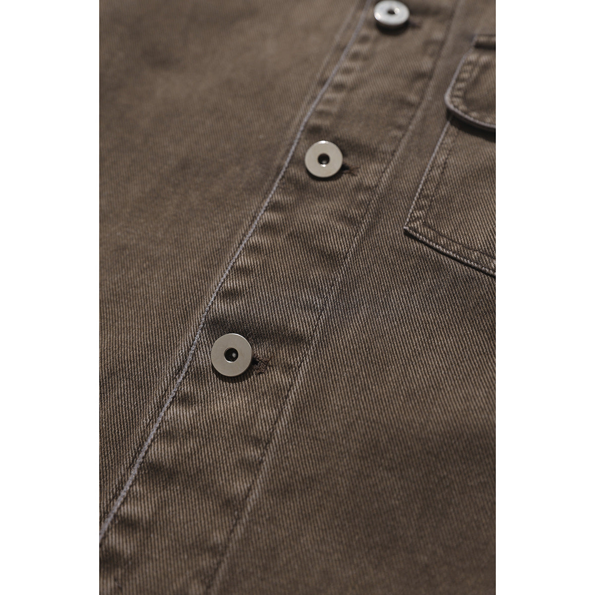Close-up of the brown shirt's button placket, showing round buttons, stitching, and fine diagonal texture.