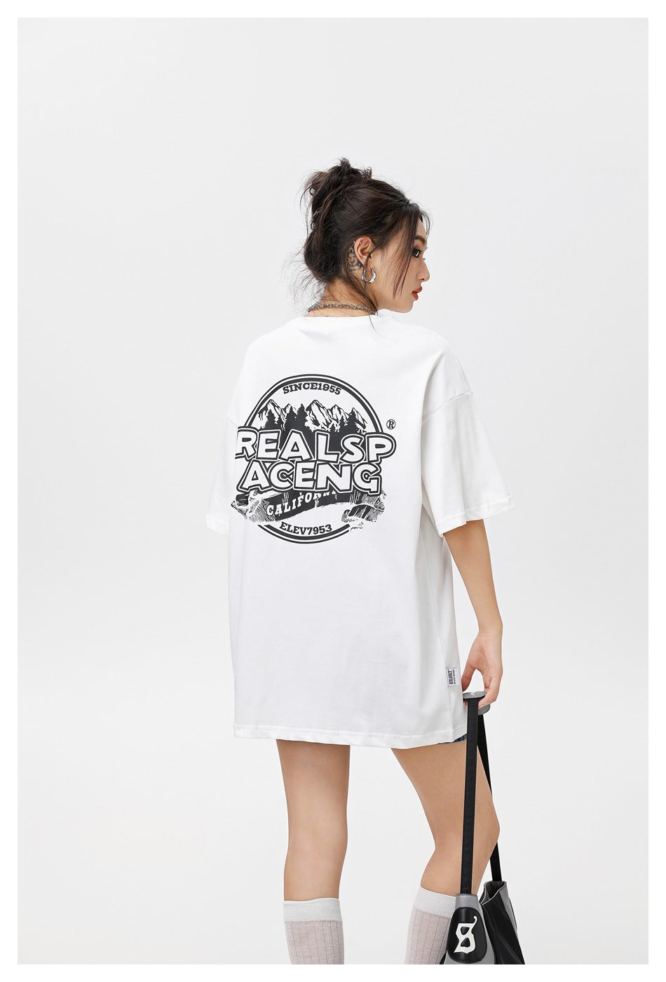 Model seen from behind wearing an oversized white T-shirt with a mountain emblem back print