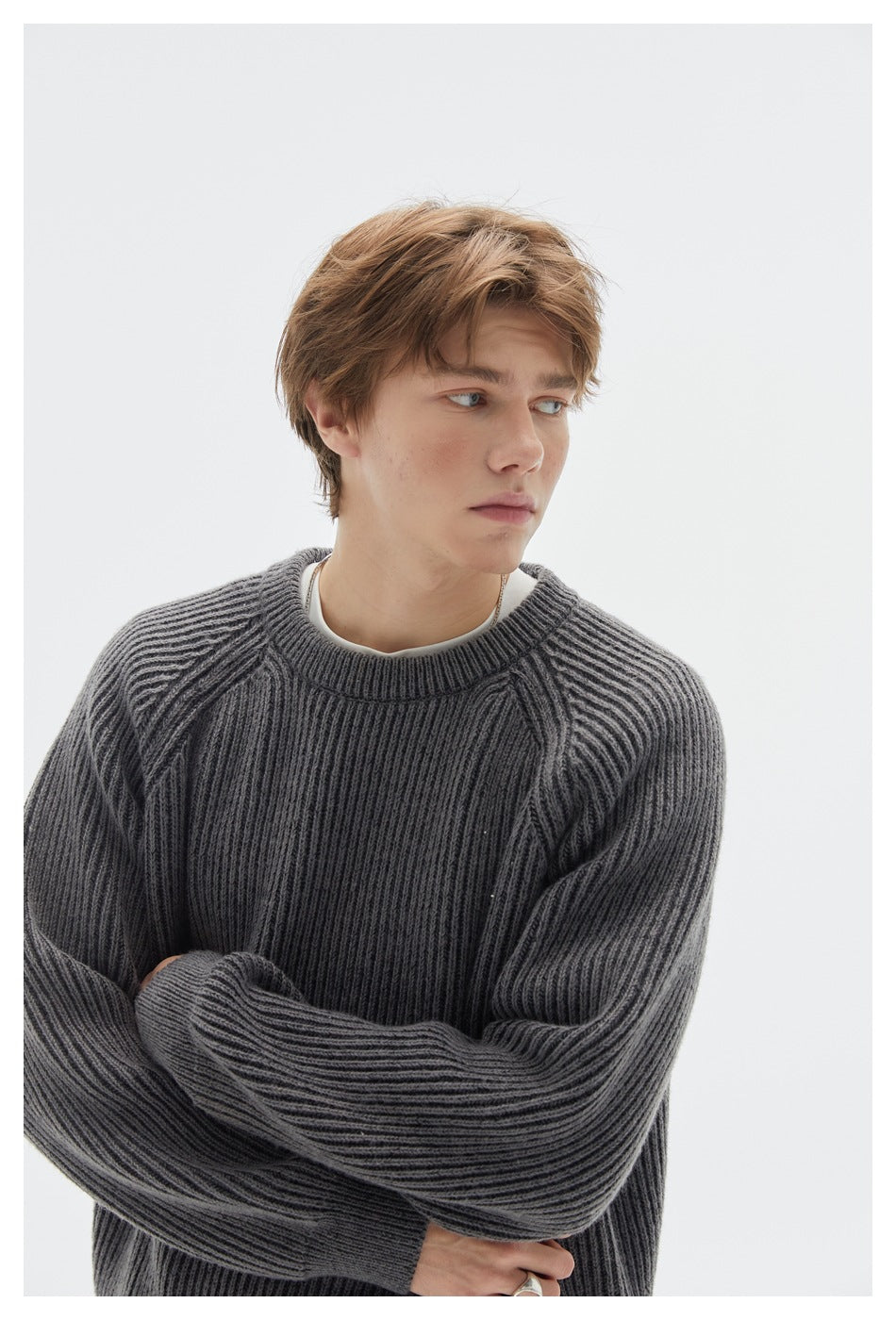 Close-up of a model wearing a charcoal ribbed crewneck sweater, showing its neckline, raglan seams, and textured knit.