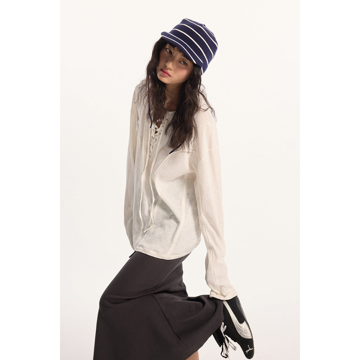 Model wearing an ivory long-sleeve lace-up top and charcoal skirt, shown with a navy striped bucket hat.